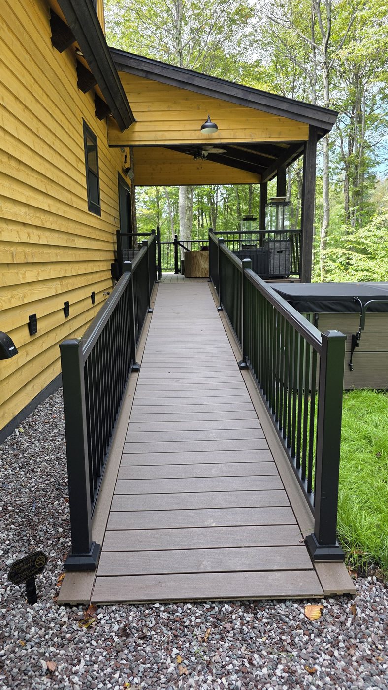 The wheelchair ramp running from the gravel driveway up to the covered deck, with railings on both sides