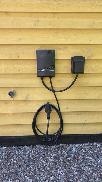 The Emporia Pro Level 2 EV charger mounted on the cedar siding, J1772 cable coiled below it