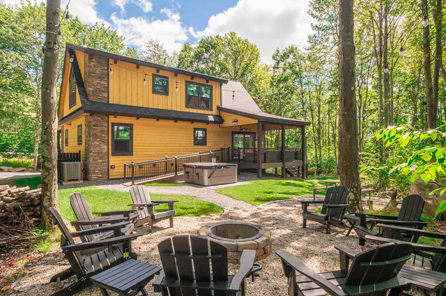 The fire pit ring with the house behind it — Adirondack chairs, the hot tub up t