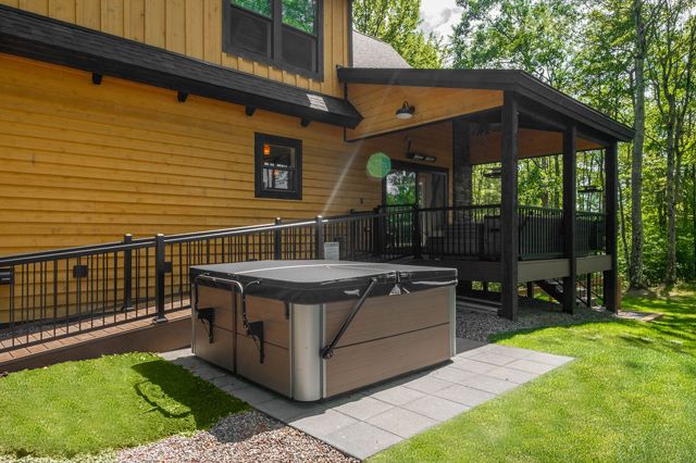 The seven-person hot tub on its own pad beside the covered deck, screened by the trees on three si