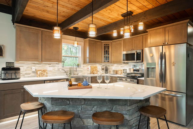 The kitchen island in stacked stone with quartz over it, amber mica pendants abo