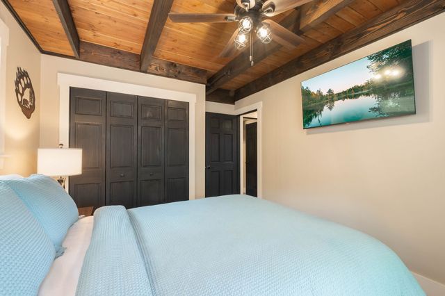 The main-floor queen from the window side, wood-plank ceiling and the woods beyo
