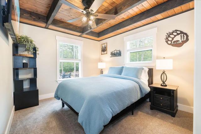 The main-floor queen guest room, wood-plank ceiling overhead and two windows int