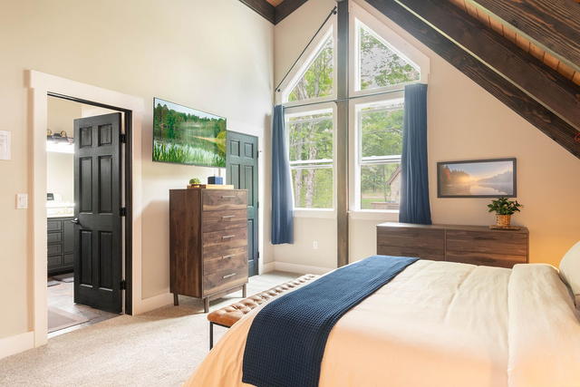 The primary suite takes the entire upper floor — a king under the timber gable, 
