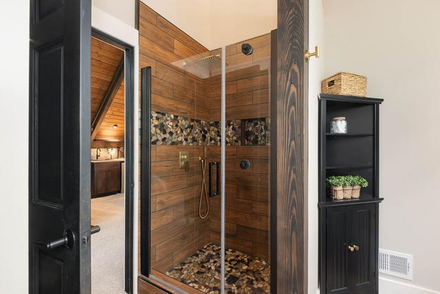 The wood-tiled walk-in shower with a rainfall head and a pebble floor, opening b